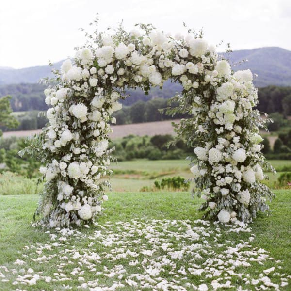White floral arch outdoors with petals scattered on grass