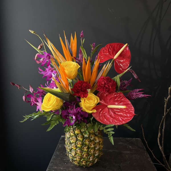 Tropical flower arrangement in a pineapple vase with red anthuriums and yellow roses