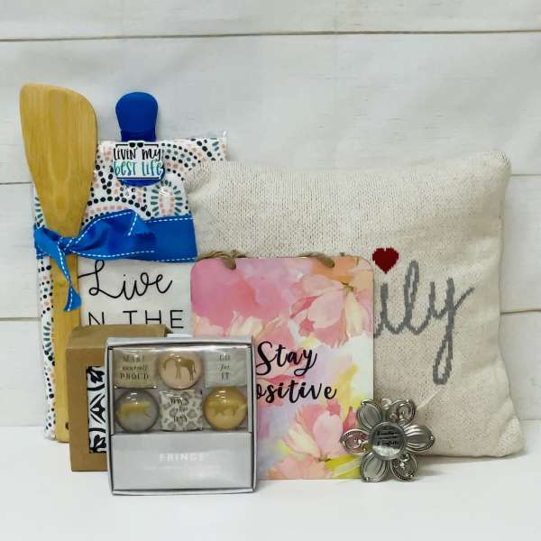 Gift set with pillow, kitchen utensils, positive message signs, and small boxed accessories.