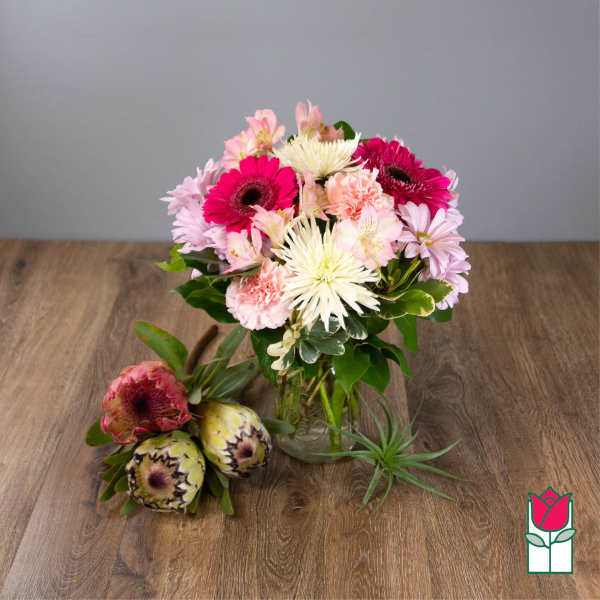 Pink and white mixed bouquet in a glass vase with two protea stems beside it.