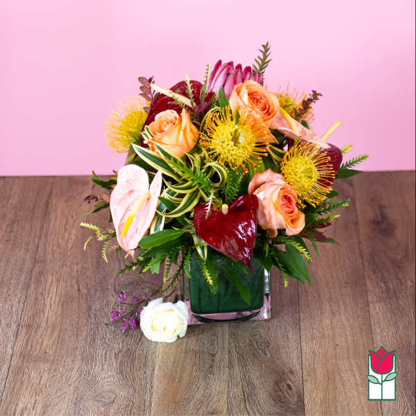 Mixed bouquet of peach roses, pink anthuriums, and yellow pincushion blooms in a glass vase.