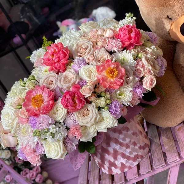 Large pastel bouquet with pink, white, and lavender flowers beside a teddy bear