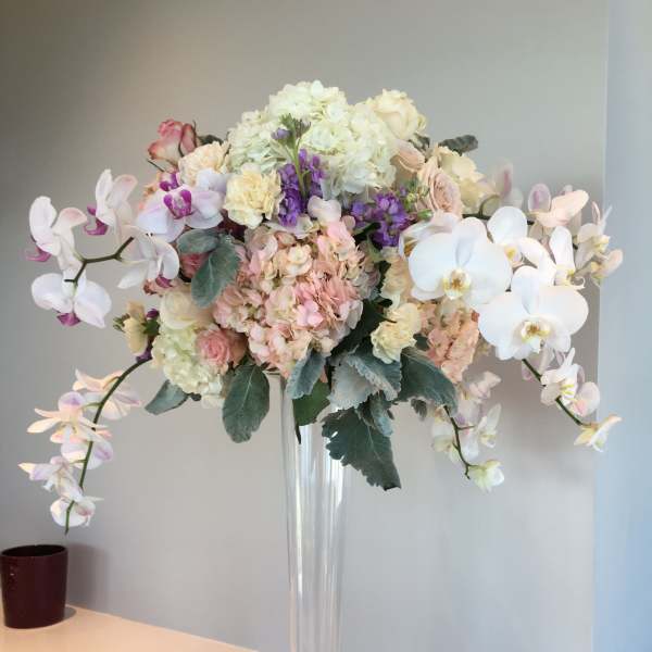 Tall pastel floral arrangement in a clear glass vase with orchids and hydrangeas