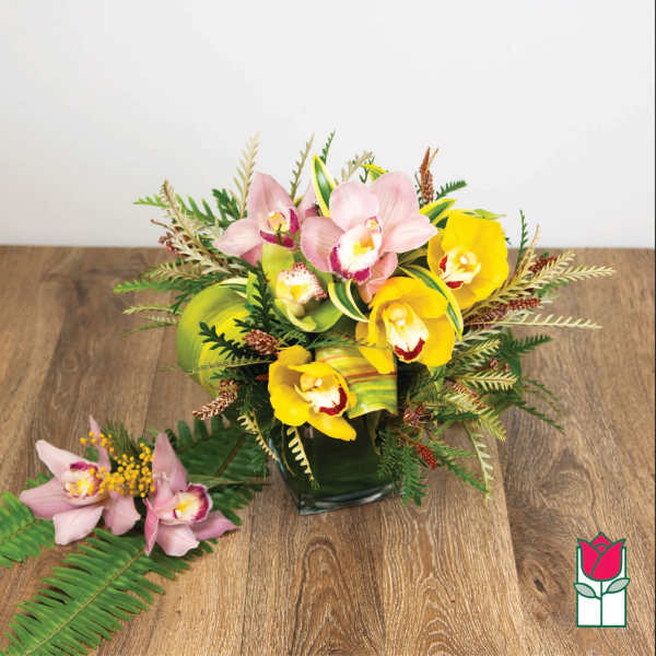 Pink and yellow orchid arrangement in a square glass vase with a matching corsage