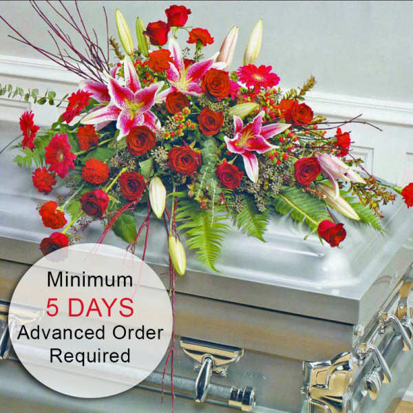 Red and pink casket spray of lilies and roses displayed on a silver casket