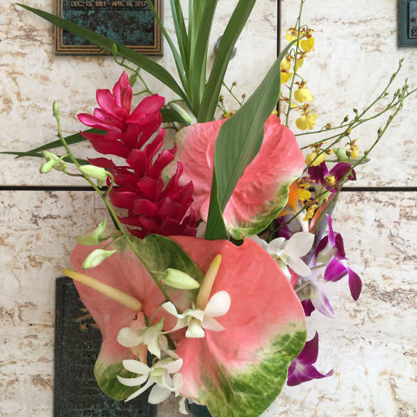 Tropical floral arrangement with pink anthuriums, orchids, and red blooms in a vase