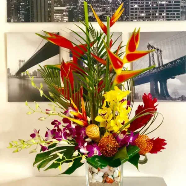 Tropical flower arrangement in a clear square vase with red, yellow, and purple blooms
