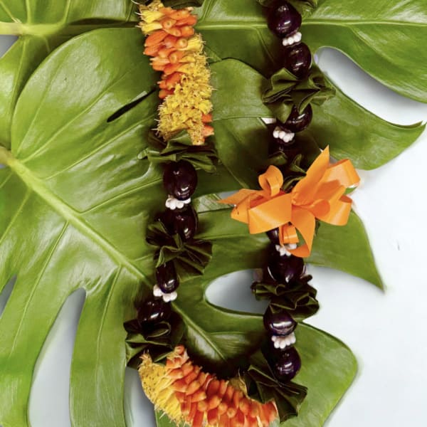 Two floral leis with orange and yellow flowers on large green leaves.