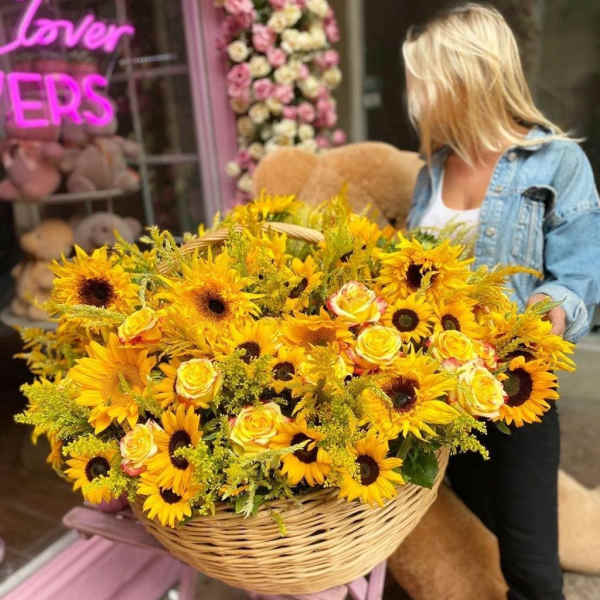 Large basket of sunflowers and yellow roses held by a woman