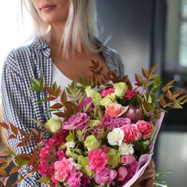 Woman holding a colorful bouquet of roses and carnations wrapped in pink paper