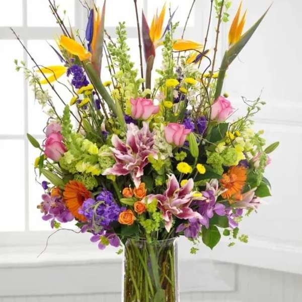 Tall mixed bouquet in a clear glass vase with pink, purple, orange, and yellow flowers