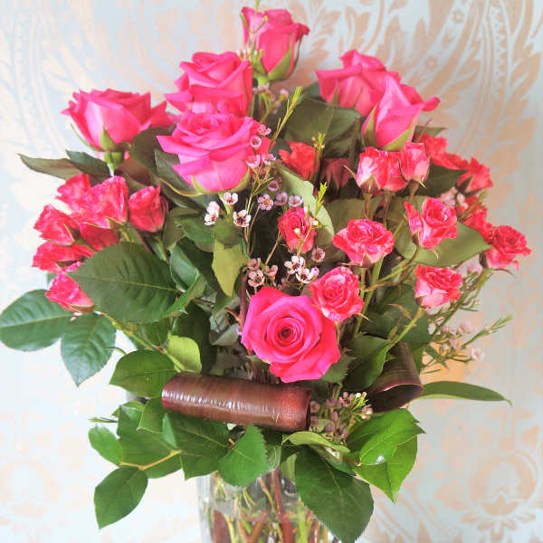 Tall bouquet of hot pink roses and spray roses in a clear glass vase