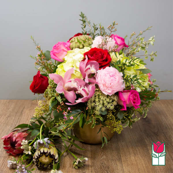 Mixed bouquet of roses, orchids, and pink blooms in a gold vase