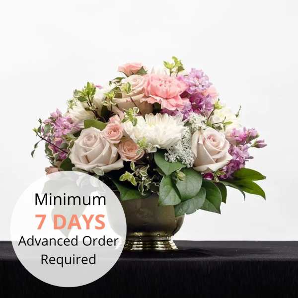 Low pastel arrangement of roses, carnations, and mums in a gold urn with a 7-day advance order text overlay.