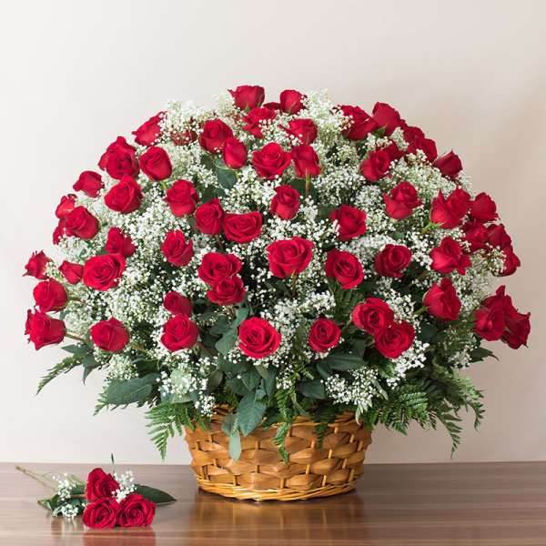 Large basket of red roses with white filler flowers and three loose roses in front