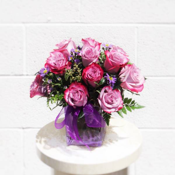 Pink roses in a purple vase with a ribbon