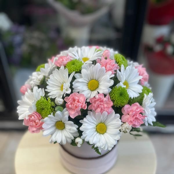 Round bouquet of white daisies and pink carnations in a pale vase