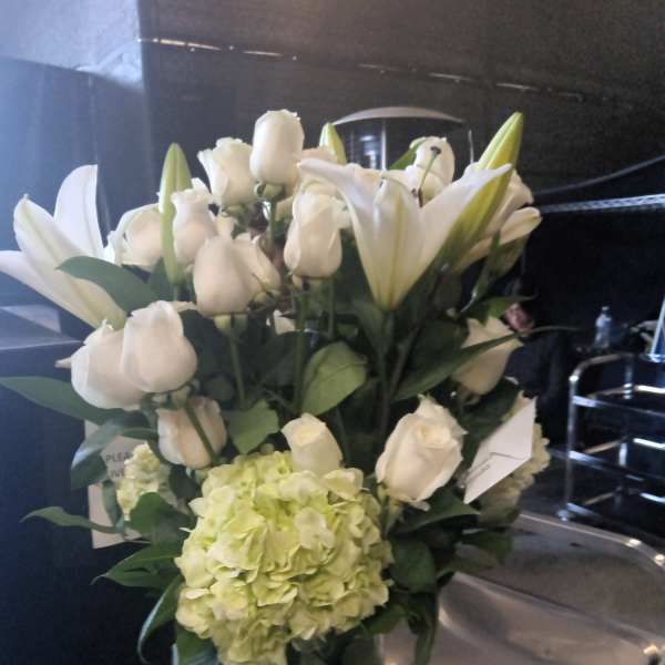 White lilies and roses in a glass vase with a pale green hydrangea bloom