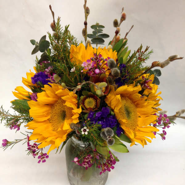 Mason jar arrangement of yellow sunflowers with purple and pink accent flowers