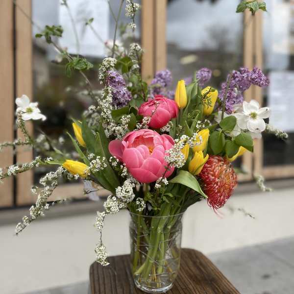 Mixed bouquet of pink peonies, yellow tulips, and white filler flowers in a glass vase