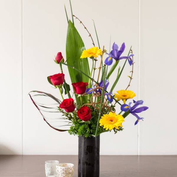Tall bouquet of red roses, yellow daisies, and purple irises in a black vase