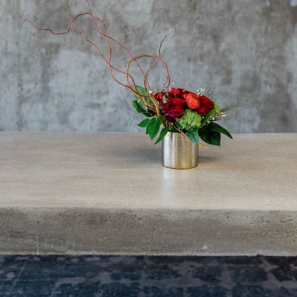 Red and orange floral arrangement in a metal vase with curly branches