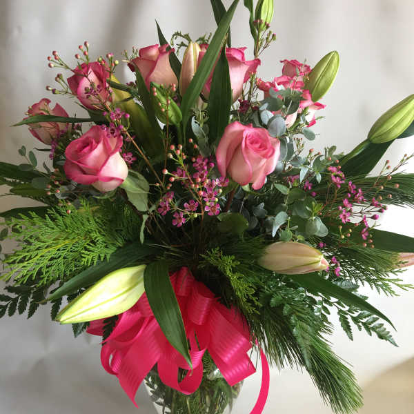 Pink roses and lilies in a glass vase with a bright ribbon