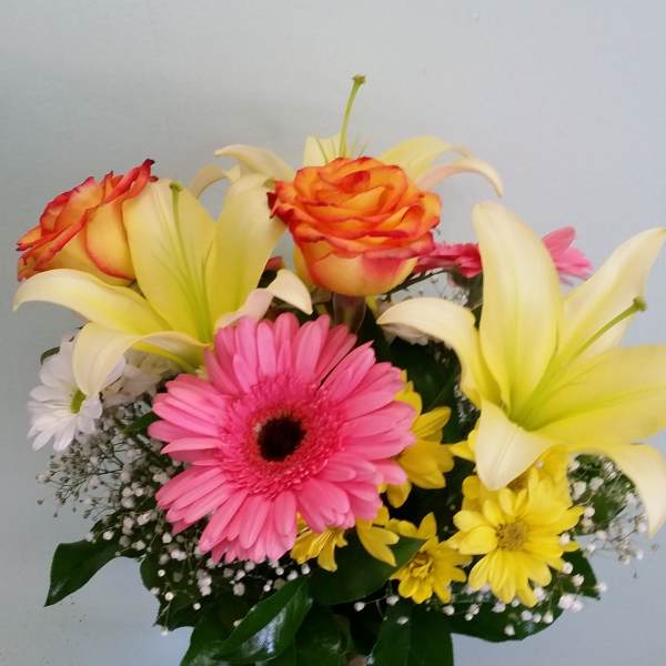 Bouquet of lilies, gerbera daisies, roses, and yellow daisies in a glass vase