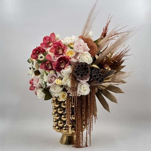 Bouquet of pink and white roses with dried grasses in a gold vase