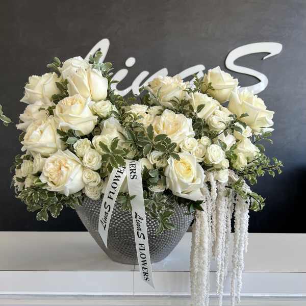 Cream rose arrangement in a textured silver vase with trailing white amaranthus