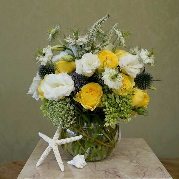 Yellow and white flower arrangement in a glass vase with a starfish accent