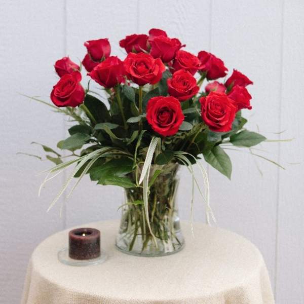 Red roses arranged in a clear glass vase beside a small candle