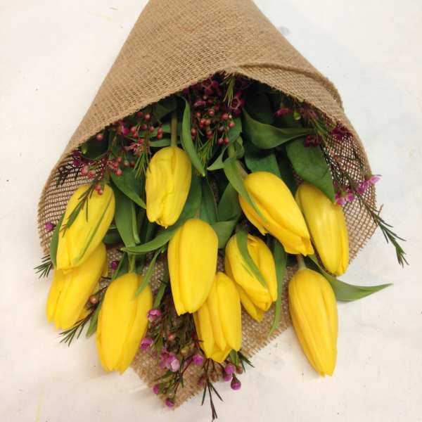 Bundle of yellow tulips wrapped in burlap with small purple flowers