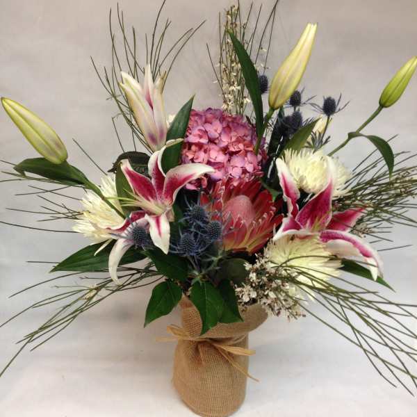 Mixed bouquet with lilies, hydrangea, and protea in a burlap-wrapped vase