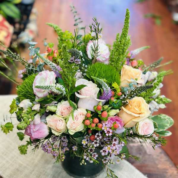 Mixed bouquet of pastel roses and small purple flowers in a dark vase
