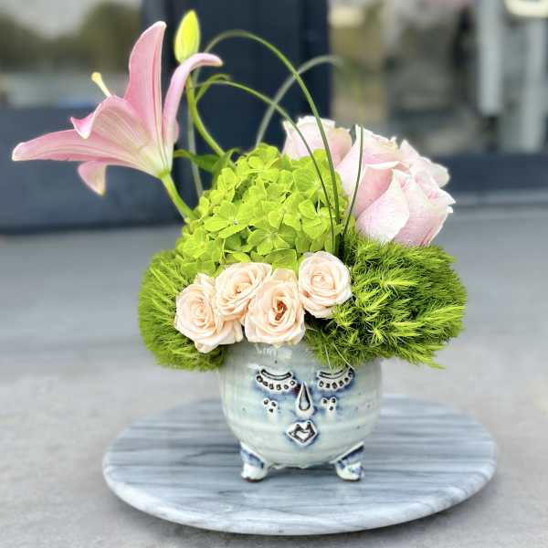 Pink lilies and roses arranged in a decorative ceramic face pot