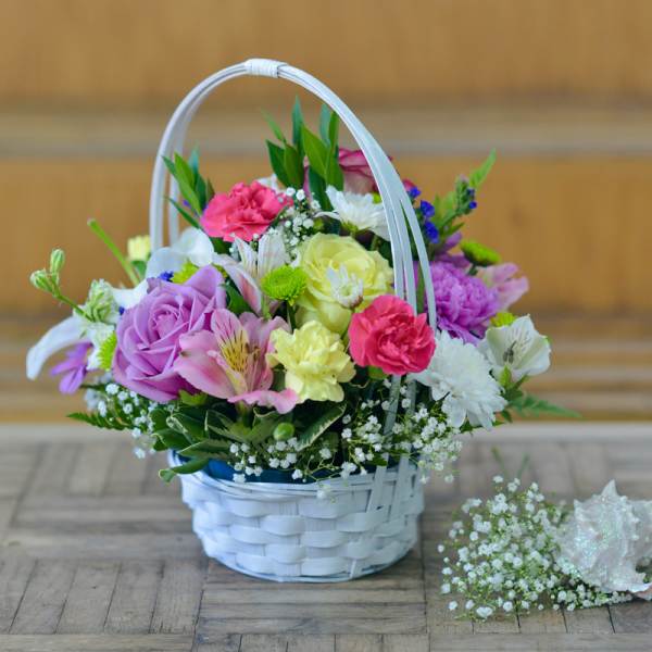 Mixed flower basket with roses, carnations, and daisies in a white wicker basket