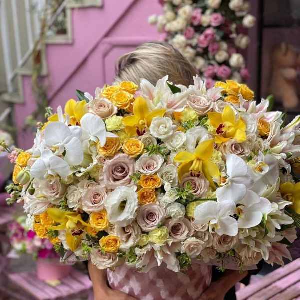 Large bouquet of white orchids, yellow orchids, and pale roses in a pink wrap