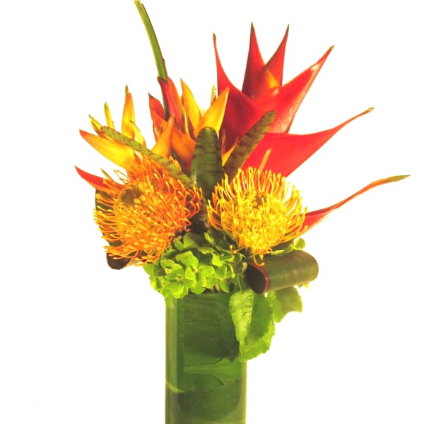 Tall tropical arrangement with orange and yellow blooms in a leaf-lined glass cylinder vase