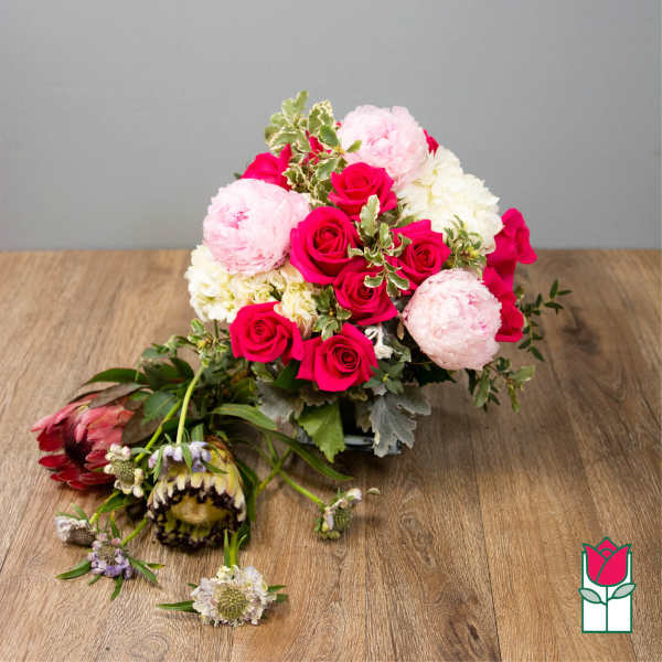 Compact arrangement of hot pink roses, pale pink peonies, and white blooms in a low glass vase.