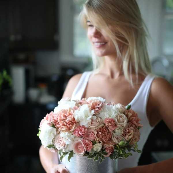 Woman holding a round pink and white rose bouquet in a silver bucket