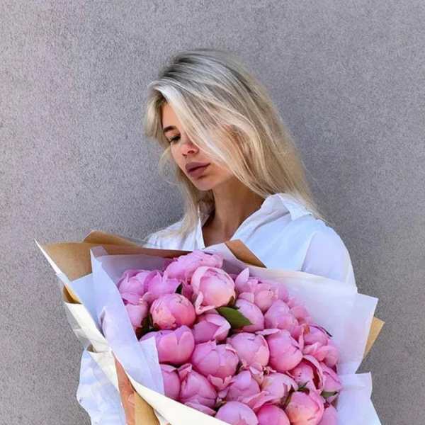 Woman holding a large bouquet of pink peonies wrapped in white paper