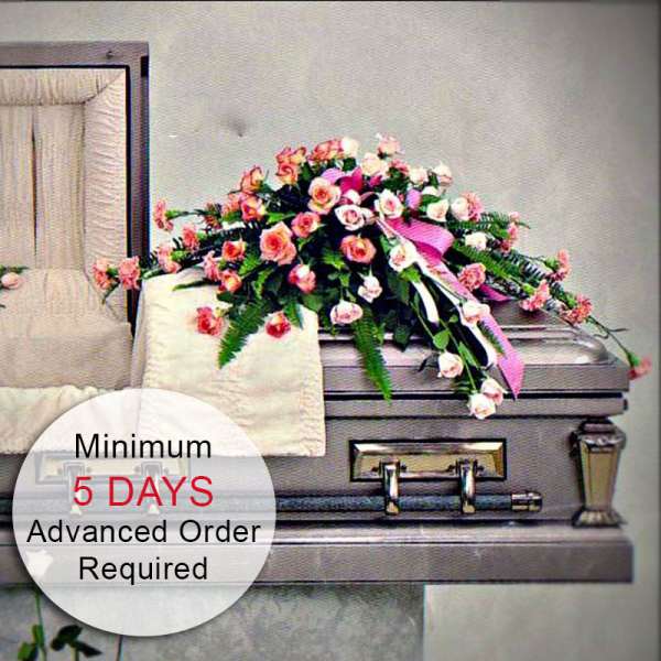 Pink and peach rose casket spray with ribbon displayed on a silver casket