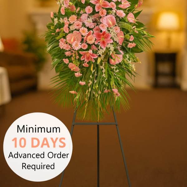 Tall pink standing spray of lilies and carnations with palm leaves on a black easel