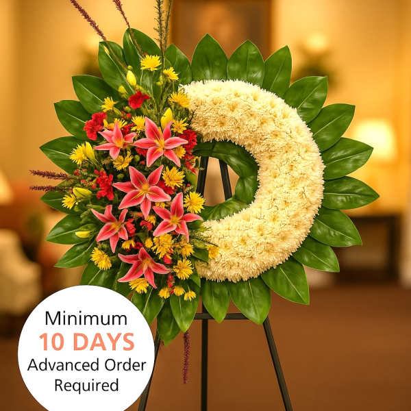 Crescent standing wreath with white blooms, pink lilies, red and yellow flowers on a green leaf base.