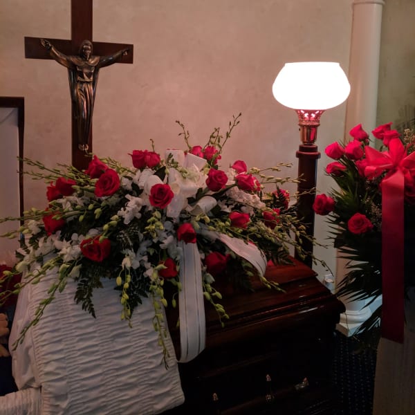 Red rose funeral spray on a casket with white ribbon and flowers