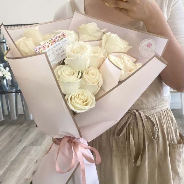 Bouquet of cream roses wrapped in pale pink paper with a ribbon