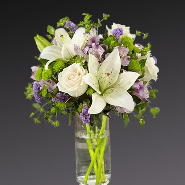 White lilies and roses in a clear glass vase with purple accents