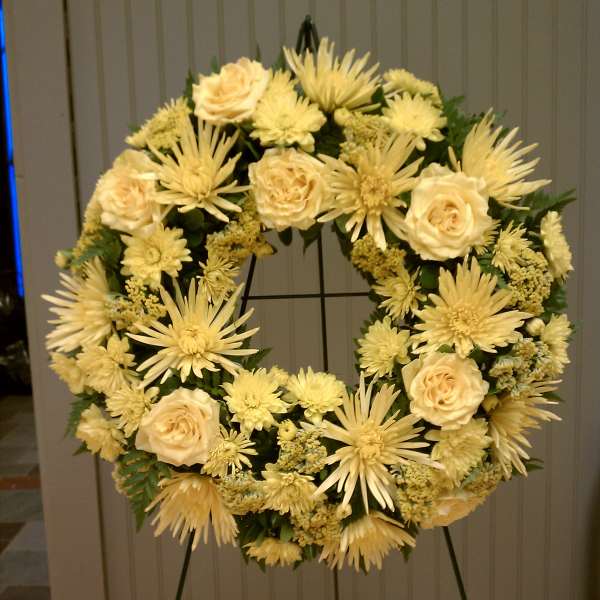Standing wreath of pale yellow roses and mums on a metal easel