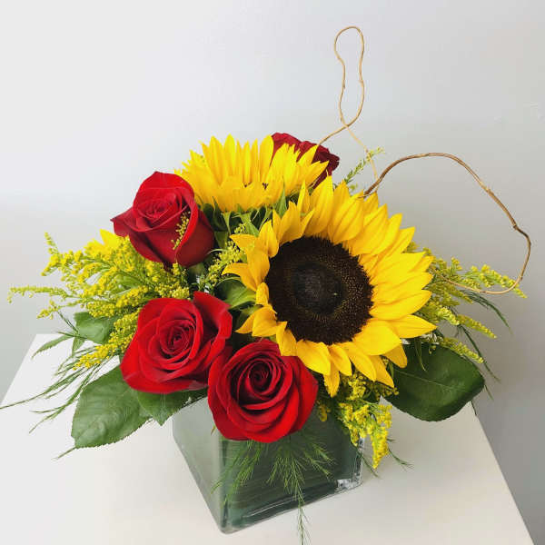 Red roses and yellow sunflowers in a square glass vase